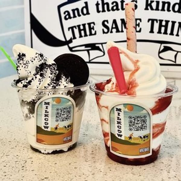 Two Milkcow soft-serve ice creams, one with Oreo and one with strawberry syrup and a wafer.