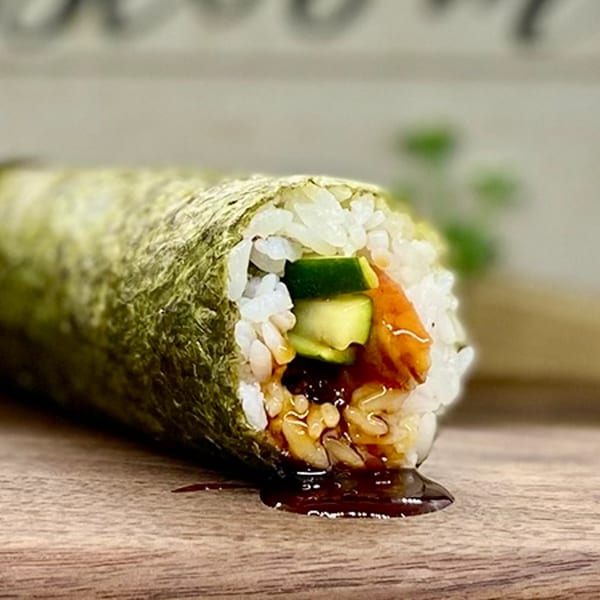 A Sunfish Poke Bar hand roll with salmon, cucumber, rice, and sauce dripping onto a wooden surface.