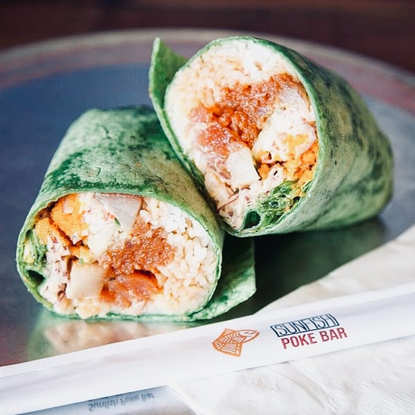 Two Sunfish Poke Bar wraps, filled with rice and orange-colored ingredients, on a metallic surface.