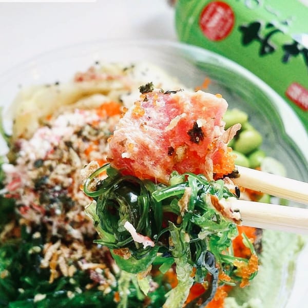Chopsticks lifting fresh tuna, seaweed, and roe from a Sunfish Poke Bar bowl.