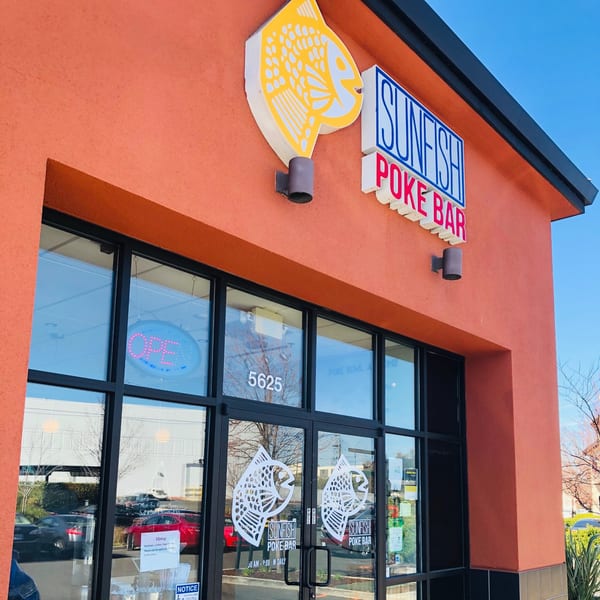 The exterior of Sunfish Poke Bar, featuring a bright orange facade with a fish logo and prominent signage.