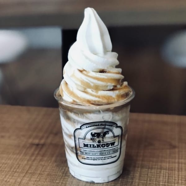 Milkcows soft serve ice cream with caramel swirls in a clear cup on a wooden table.